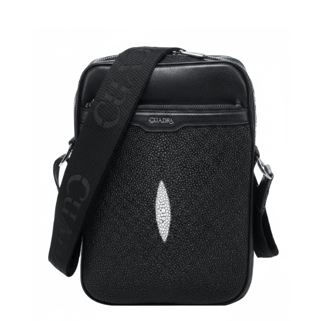 Bolso bandolera negro con textura de mantarraya y detalle central claro.