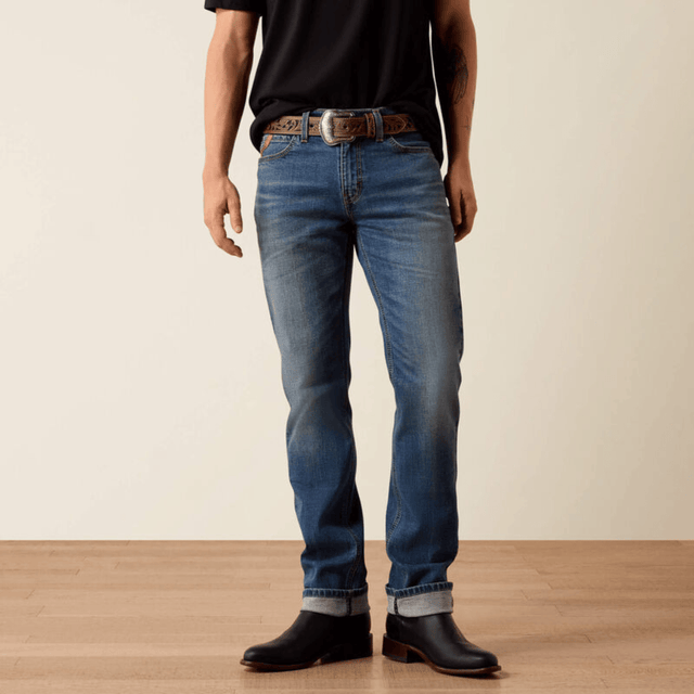 Vista frontal de jeans slim azul con botas negras y cinturón.
