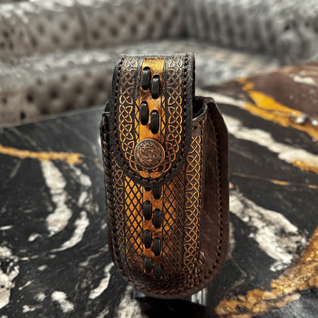 Funda de piel vista de frente con detalles grabados y concho metálico.