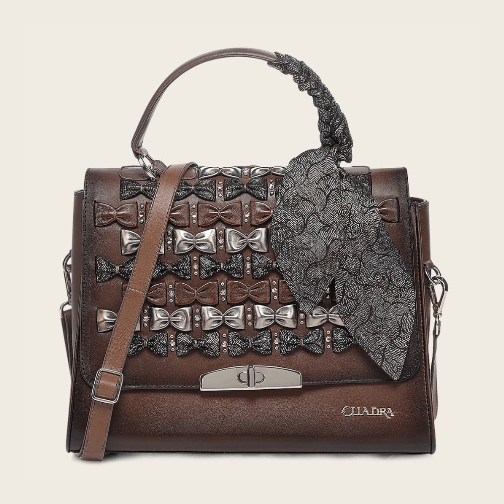 Vista frontal del bolso en piel café decorado con moños metálicos.