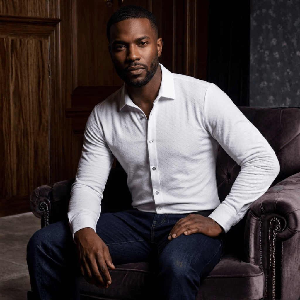 Hombre sentado con camisa blanca, look elegante y relajado.